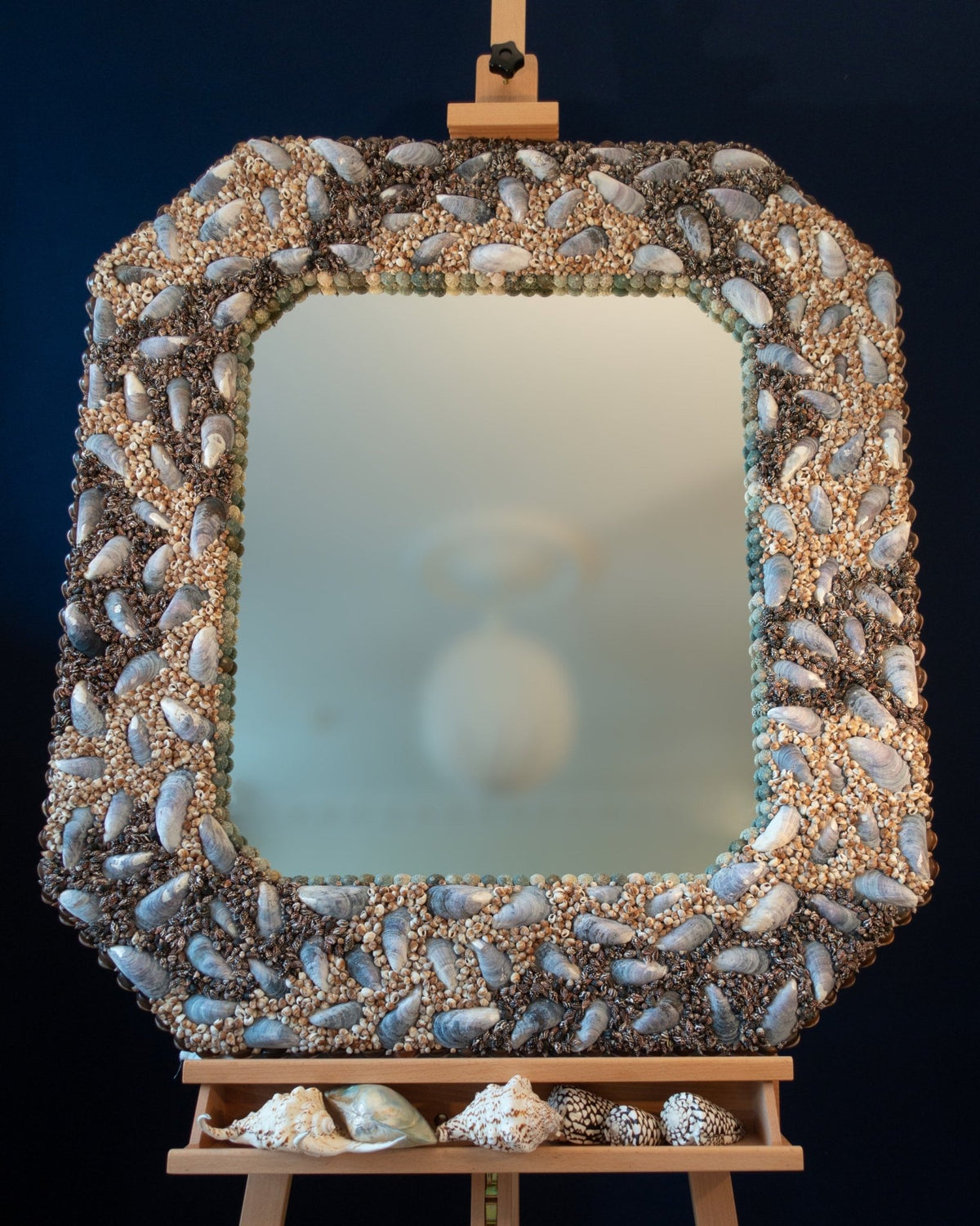 Cutting Corners Skaret octagonal shell mirror on a wooden easel against a deep blue background