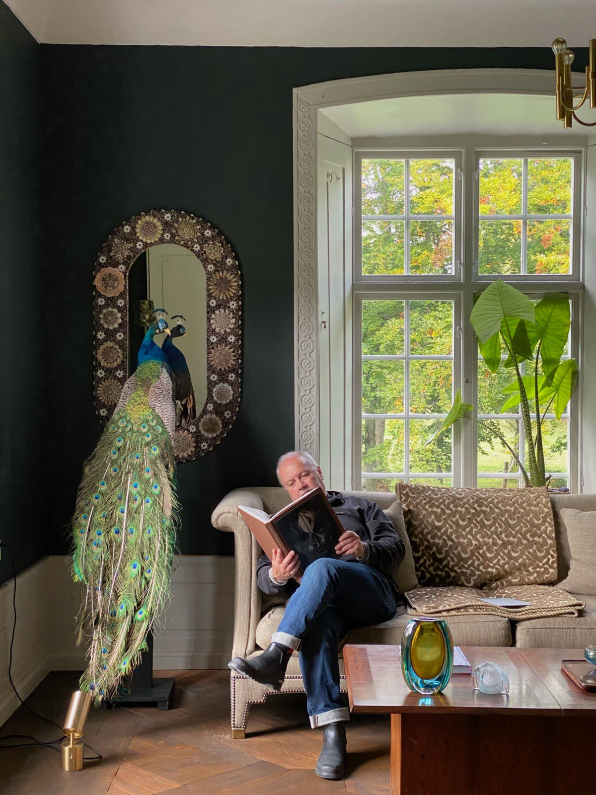 The Flower Power shell mirror on a dark green wall above a peacock in the Kåseholm main house