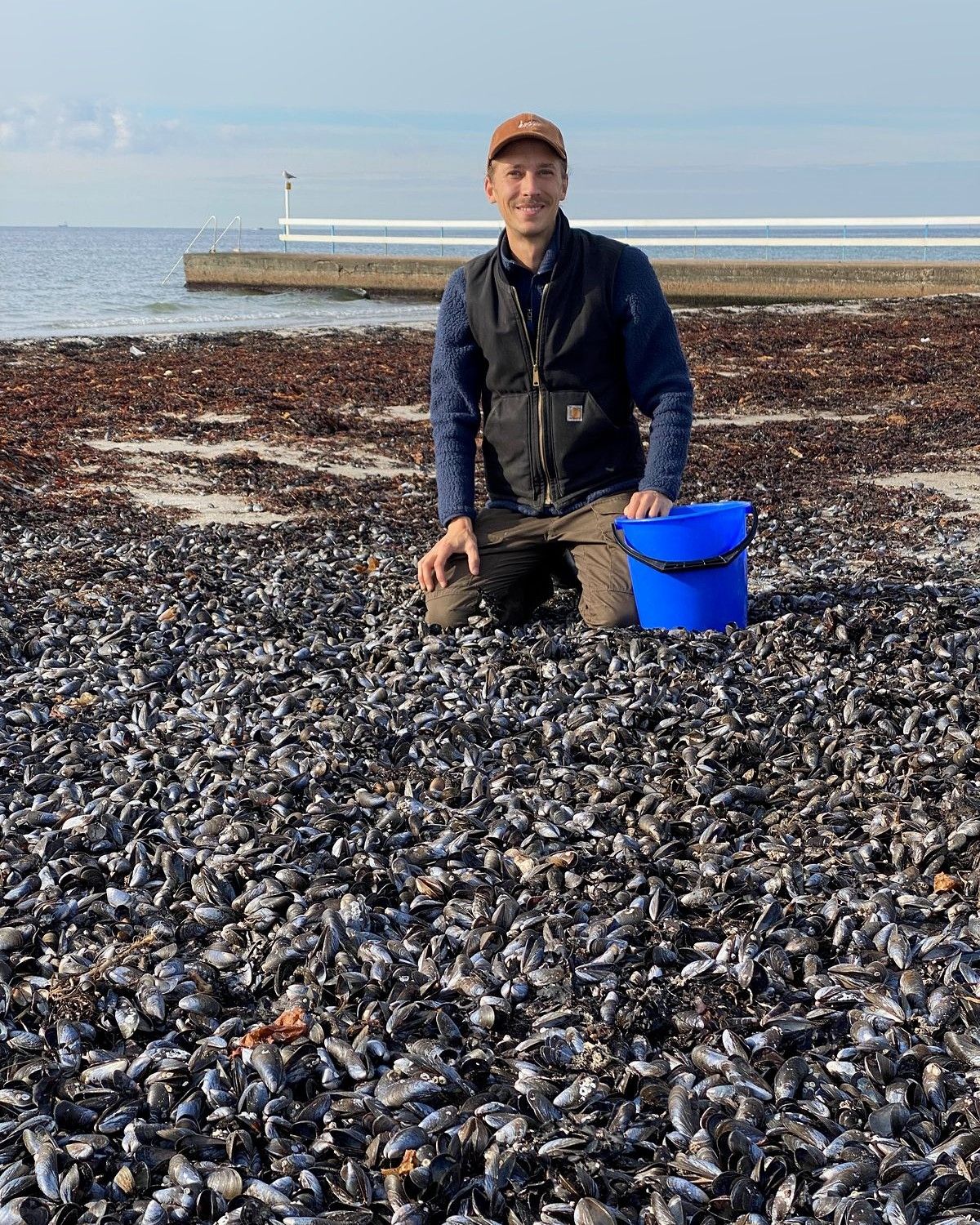 Buster Eriksson kneeling on a beach covered in blue mussel shells, collecting shells for The Flow