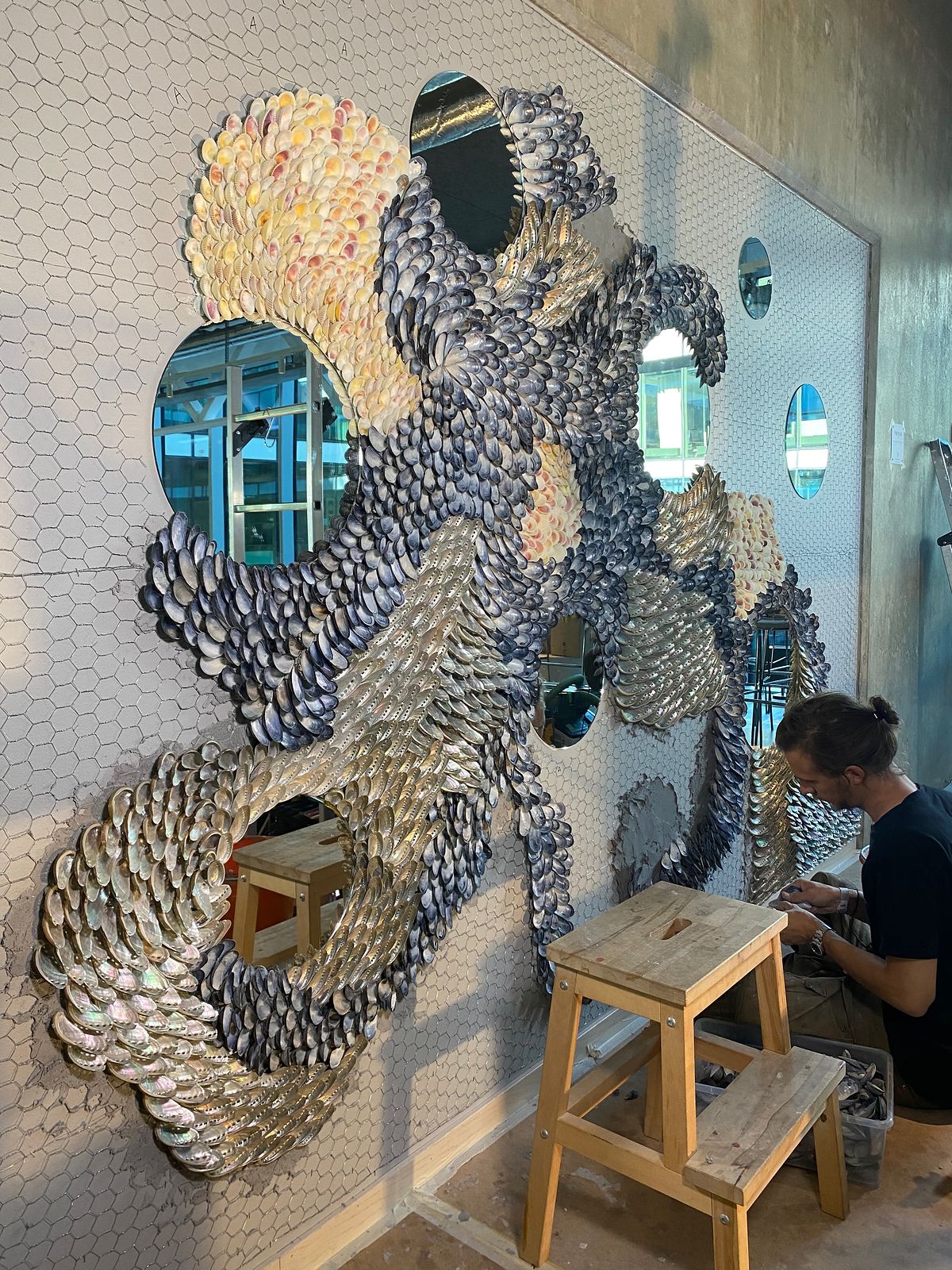 The first shell sections and round mirrors on the mesh-covered wall, Mikael Hjärtsjö working on a stool