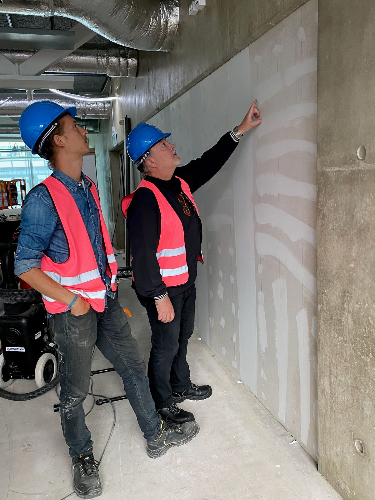Buster Eriksson and Mikael Hjärtsjö in hard hats studying the bare concrete wall on the twelfth floor of Platinan, September 2021