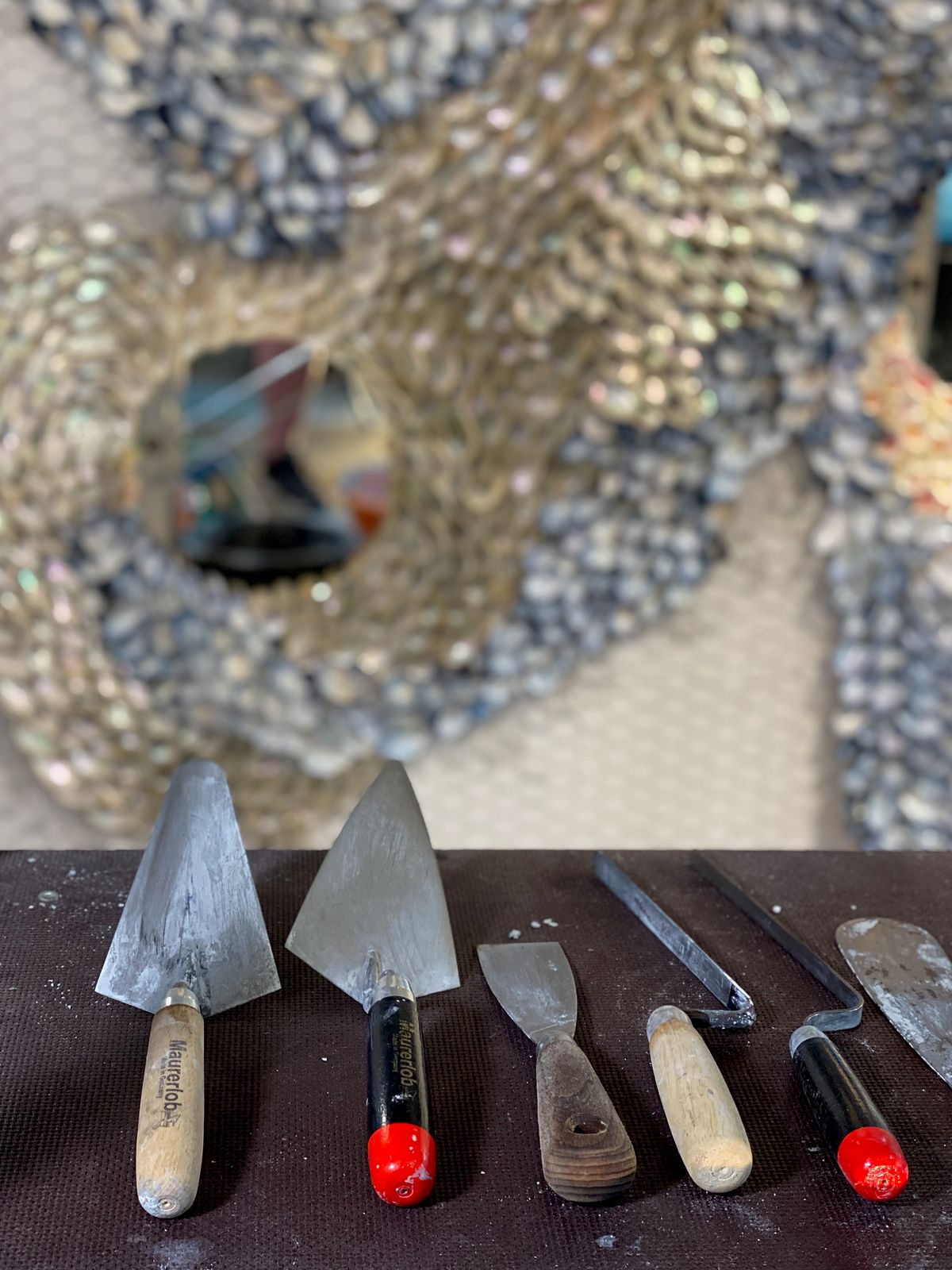 Trowels and palette knives on a table below a shell-framed round mirror